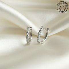 Silver hoop earrings with embedded stones on a satin surface, featuring 'Real Sterling Silver' certification.