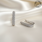 Silver hoop earrings with AAA+ CZ Zircons on a soft beige background, featuring 'Real Sterling Silver' stamp.