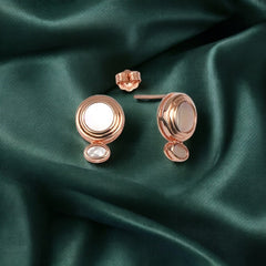 A pair of rose gold-colored sterling silver stud earrings with mother of pearl inlay, displayed on a green satin background.