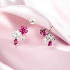 A pair of 925 sterling silver earrings with a purple blossom design, featuring pink and clear stones, displayed on a pink surface.