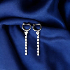 A pair of 925 sterling silver hoop earrings with a heart design, featuring rhodium plating and adorned with high-quality AAA+ CZ Zircons, displayed on a blue fabric background.
