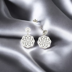 A pair of sterling silver dangler earrings with sparkling zircon stones, displayed on a silky grey background.