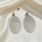 Silver earrings with honeycomb pattern on a white fabric background
