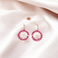 A pair of rosegold floral earrings with pink zircon stones, displayed on a silky surface.