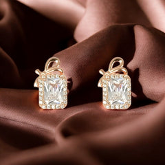 A pair of rose gold emerald cut stud earrings with a bow design and halo of cubic zirconia stones,
