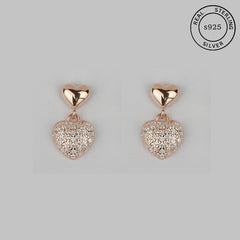 A pair of rose gold-tone heart-shaped dangle earrings with cubic zirconia embellishments on a white background.