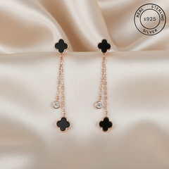 Pair of black clover-shaped earrings with rose gold chains featuring 'Real Sterling Silver' stamp.