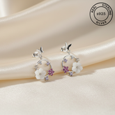 Silver earrings with floral designs and gemstones on a soft fabric background, labeled as real sterling silver.