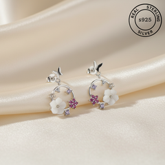 Silver earrings with floral designs and gemstones on a soft fabric background, labeled as real sterling silver.