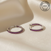 Silver hoop earrings with pink gemstones on a beige surface, featuring 'Real Sterling Silver' certification.