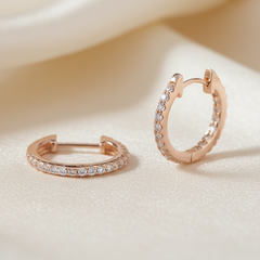 Rose gold hoop earrings with embedded diamonds on a beige background