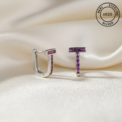 Silver earrings with purple gemstones on a white fabric background, featuring 'Real Sterling Silver s925' label.