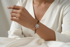 Woman wearing a bracelet with a white flower design on a plain background