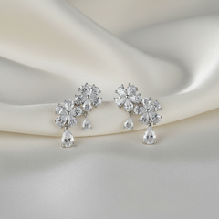 Pair of silver earrings with clear gemstones on a soft white fabric background