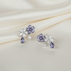 Pair of floral earrings with purple gemstones on a soft fabric background
