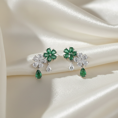 Pair of earrings with green gemstones and clear stones on a satin surface
