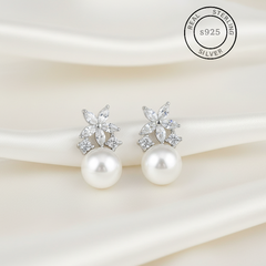 Pearl earrings with silver floral tops on a soft fabric background, featuring 'Real Sterling Silver' stamp.