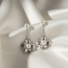 Silver flower-shaped earrings with pearl centers on a white satin background