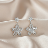 Starfish-shaped earrings with gemstones on a beige fabric background