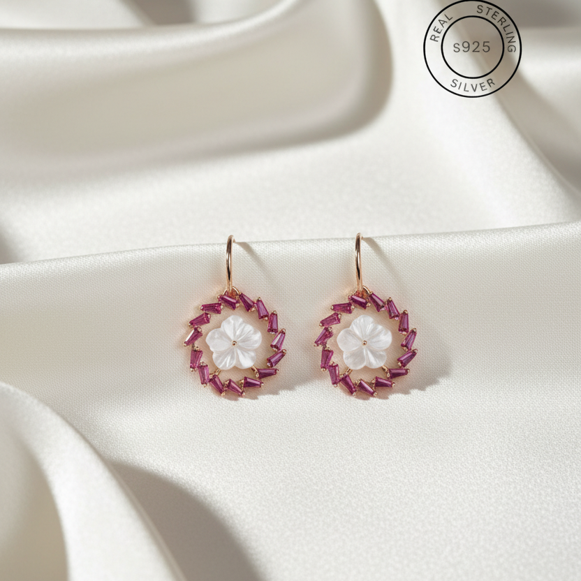 Pair of earrings with pink and white floral designs on a white fabric background