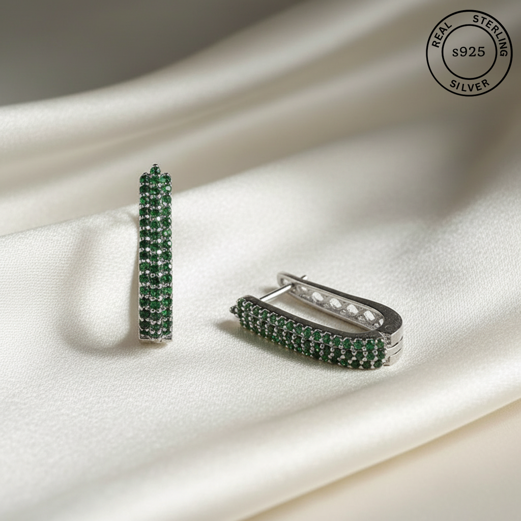 Silver earrings with green gemstones on a white fabric background, featuring 'Real Sterling Silver' stamp.