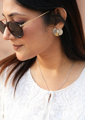 A woman wearing sunglasses and silver pearl textured earstuds.