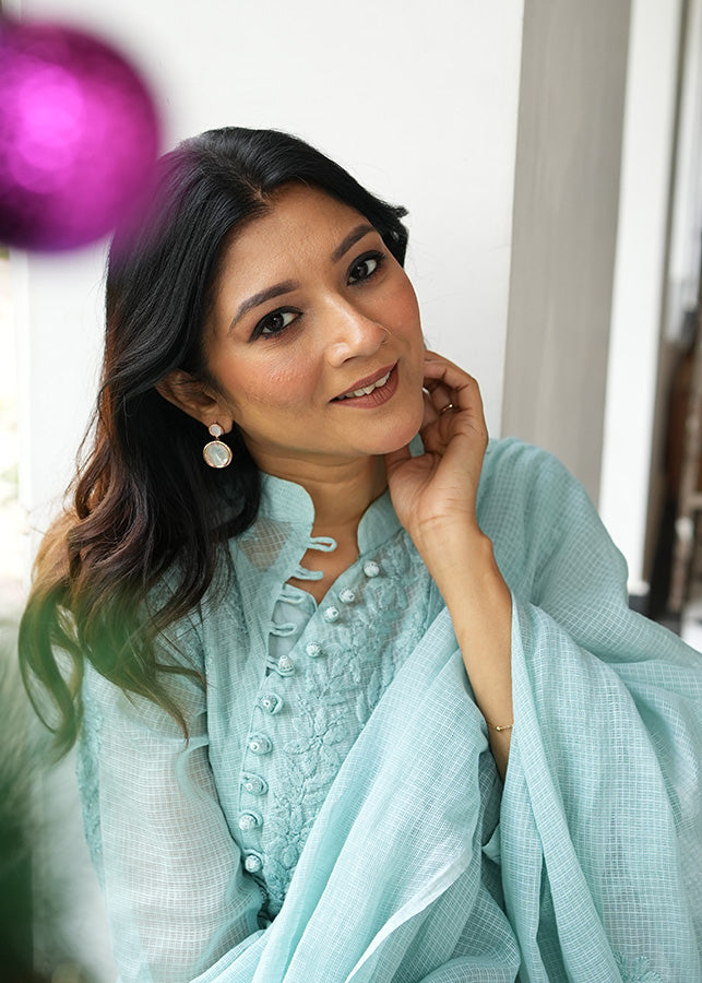 A woman wearing rosegold-colored earrings with mother of pearl dangles, smiling and sitting in a relaxed pose.