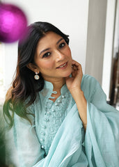 A woman wearing rosegold-colored earrings with mother of pearl dangles, smiling and sitting in a relaxed pose.