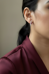 Close-up of a person wearing a silver earring with a red gemstone against a neutral background