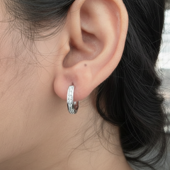 Close-up of an ear wearing a silver hoop earring with small stones.