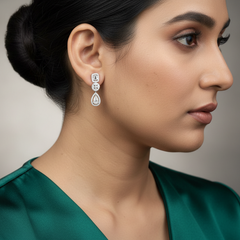 Woman wearing a pair of earrings with a green top against a neutral background