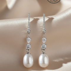 Pearl and silver drop earrings on a soft beige background