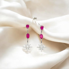 A pair of silver dangle earrings with pink star-shaped zircon stones, displayed on a white silky surface.