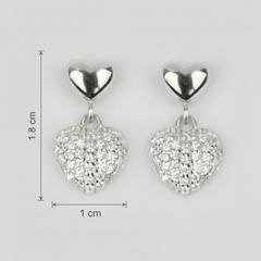 Heart-shaped silver earrings with clear stones and measurements on a light gray background