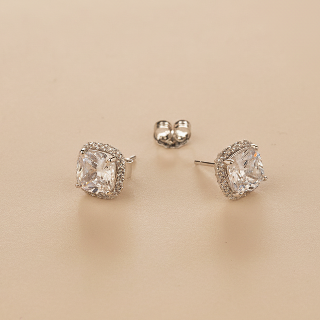 Pair of silver stud earrings with AAA+ CZ gemstones on a beige background