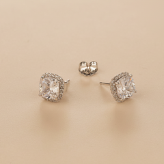 Pair of silver stud earrings with AAA+ CZ gemstones on a beige background