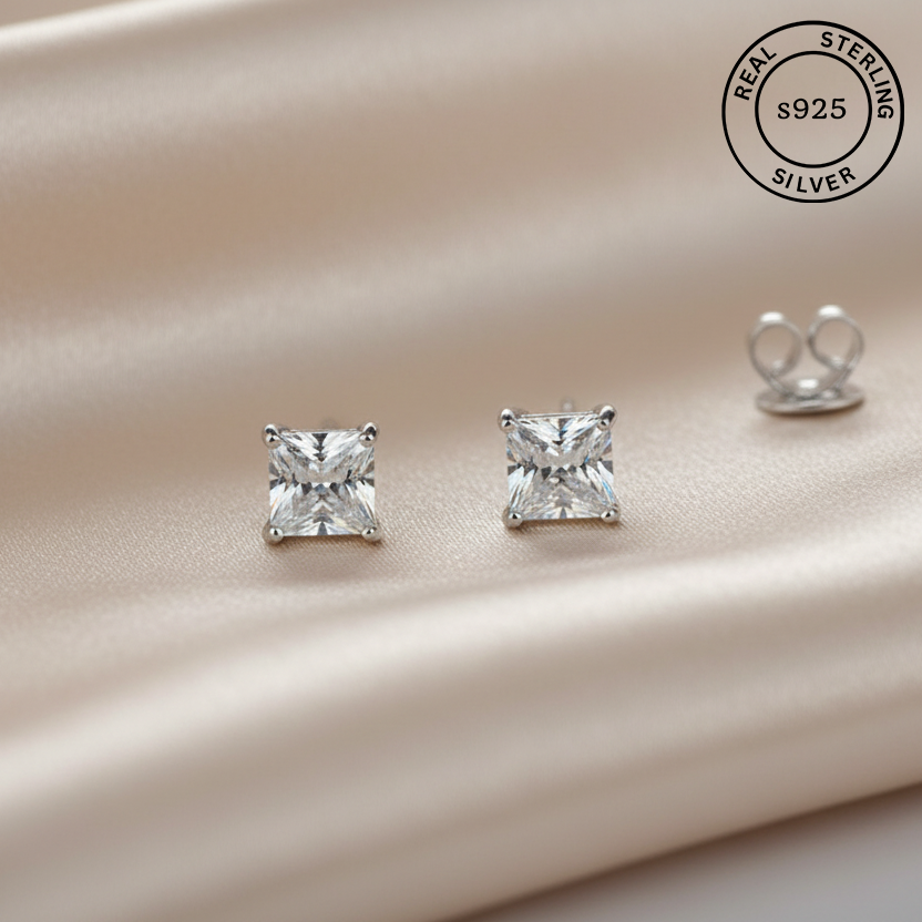 Pair of silver square-cut stud earrings on a satin surface with 'Real Sterling Silver 925' stamp.