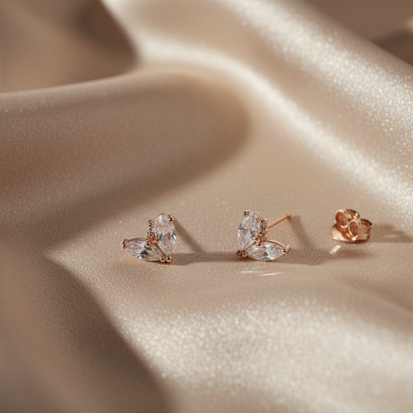 Rose gold heart-shaped earrings on a beige fabric background