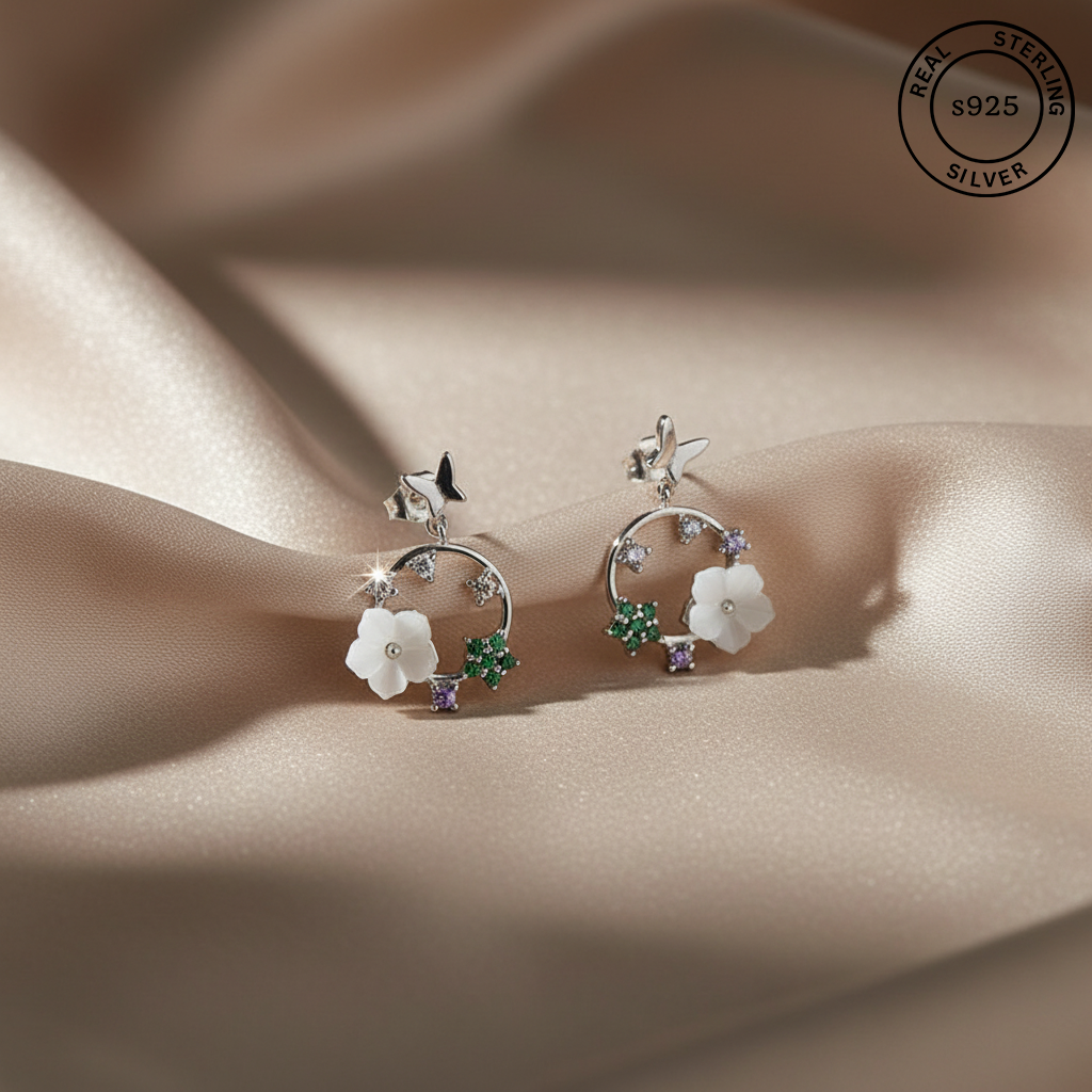 Pair of silver earrings with floral designs on a beige fabric background, featuring 'Real Sterling Silver' stamp.