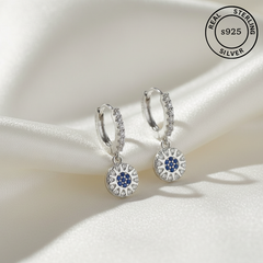 Silver hoop earrings with blue gemstones on a white fabric background, featuring 'Real Sterling S925' label.