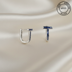 Silver hoop earrings with blue gemstones on a satin surface, featuring 'Real Sterling Silver s925' label.