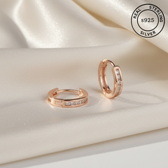 Rose gold hoop earrings with embedded stones on a satin surface, featuring 'Real Sterling Silver' 925 stamp.