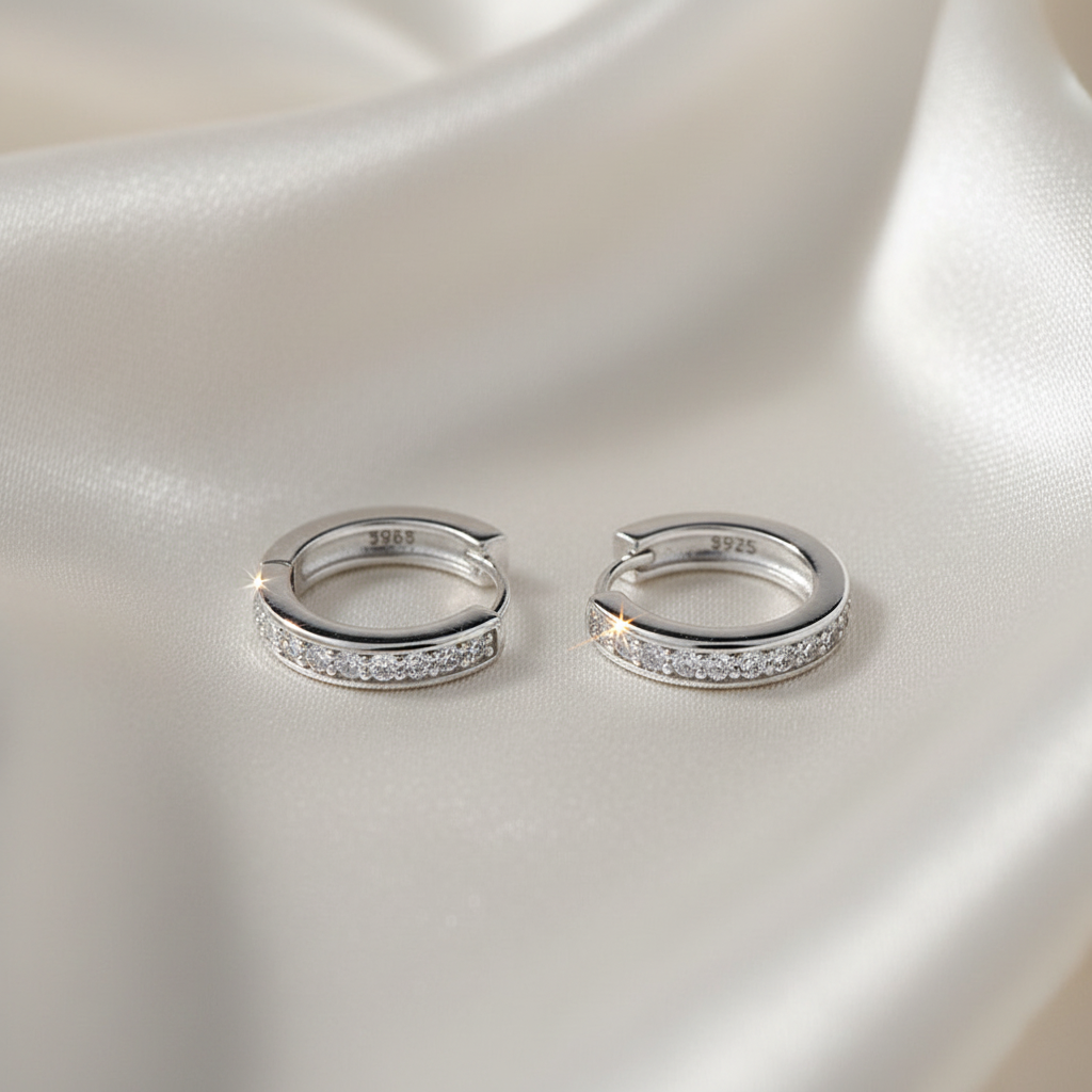 Pair of silver hoop earrings with embedded stones on a satin surface
