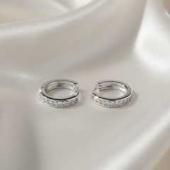 Pair of silver hoop earrings with embedded stones on a satin surface