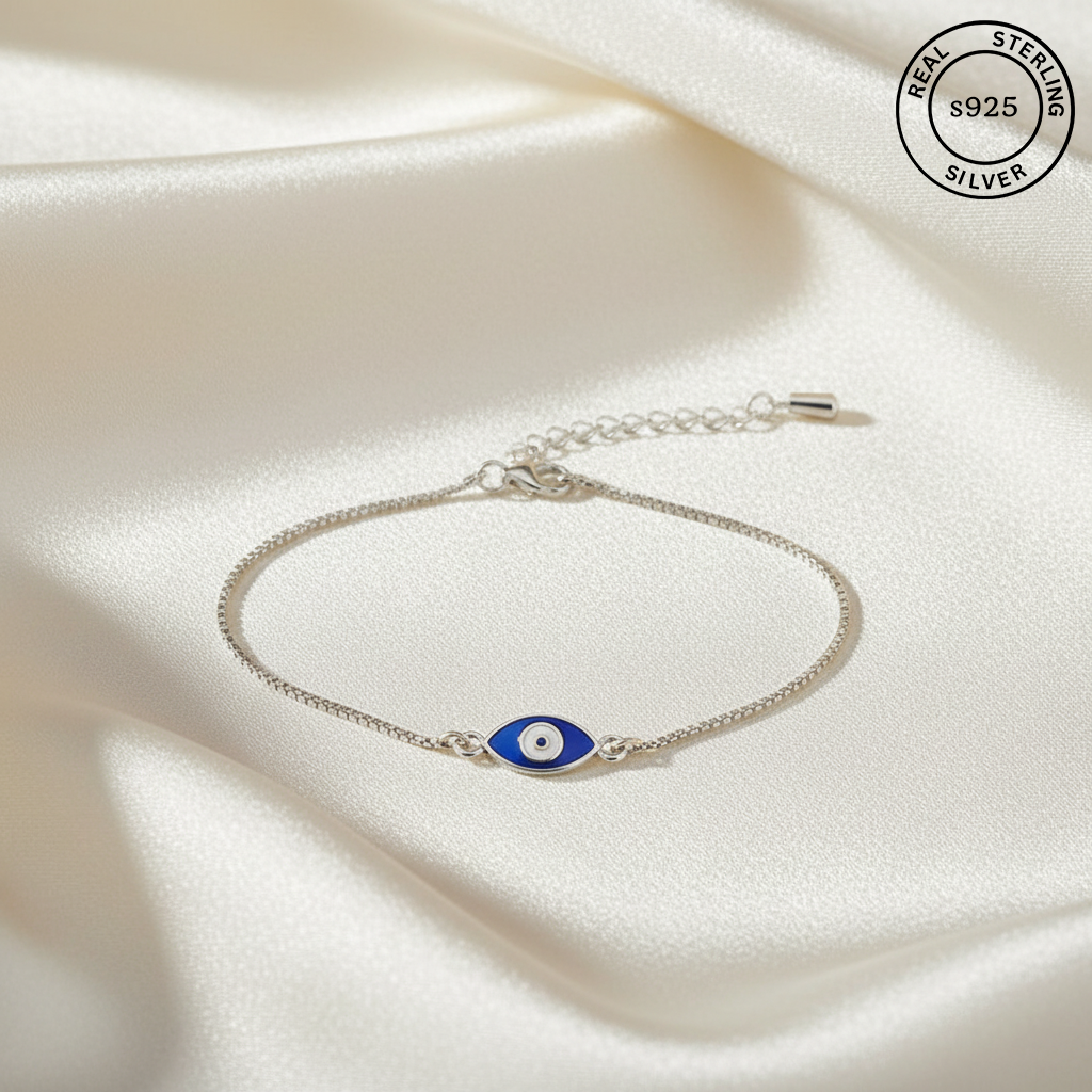 Silver bracelet with a blue evil eye charm on a white fabric background, featuring 'Real Sterling Silver' stamp.