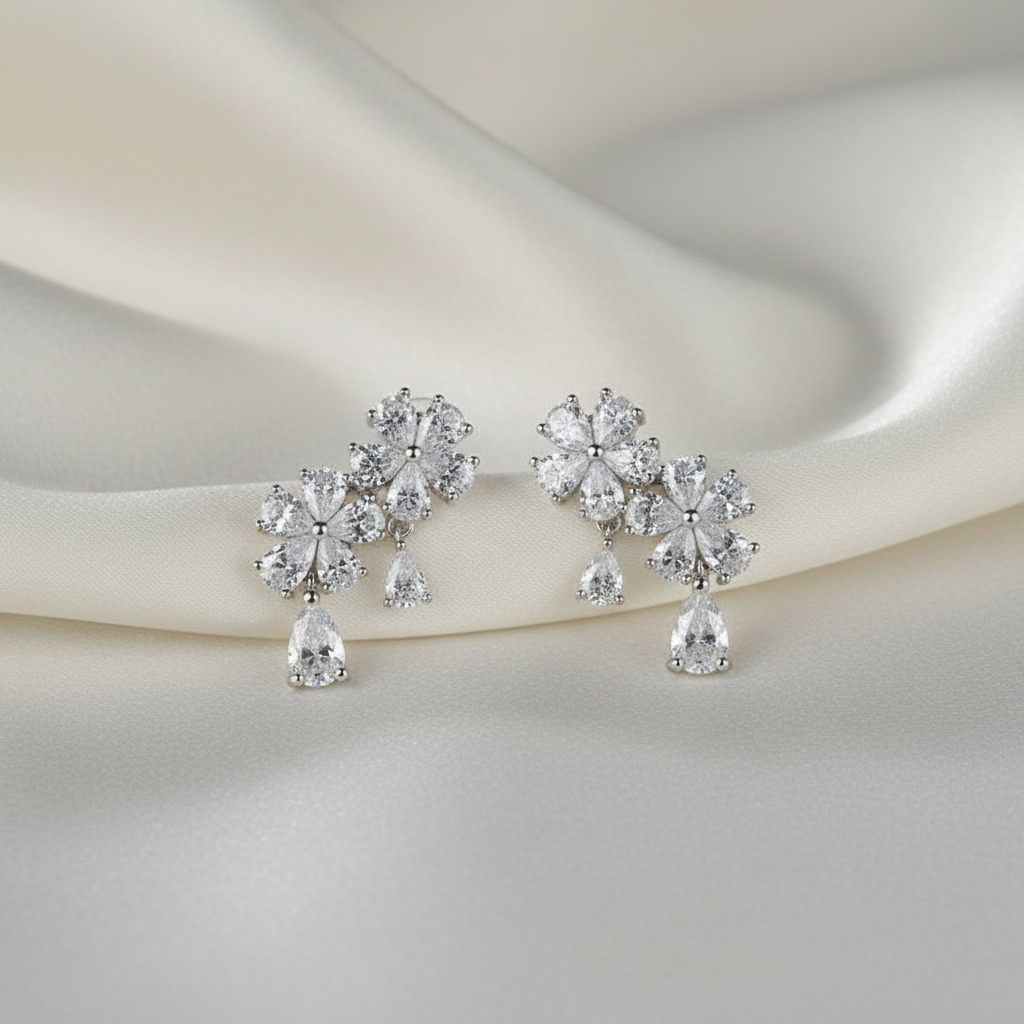 Pair of silver earrings with clear gemstones on a soft white fabric background