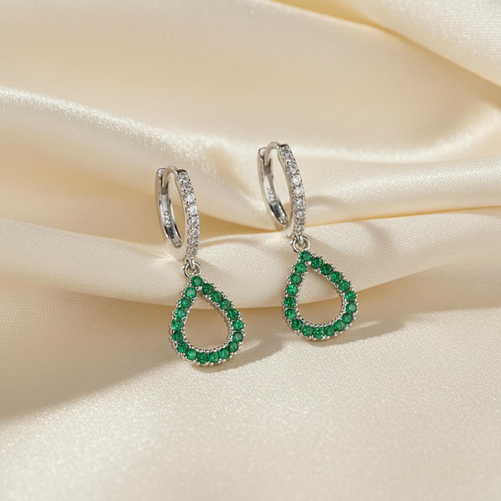 Pair of emerald teardrop earrings on a beige fabric background