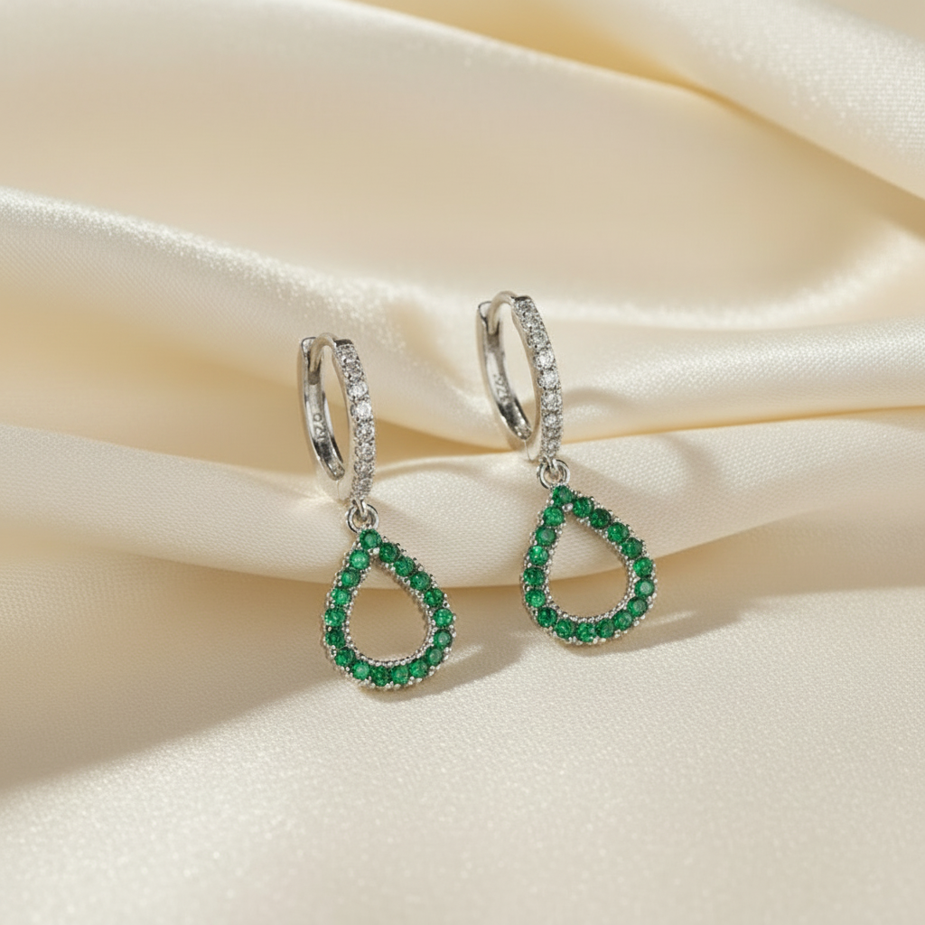 Pair of emerald green teardrop earrings on a beige satin background