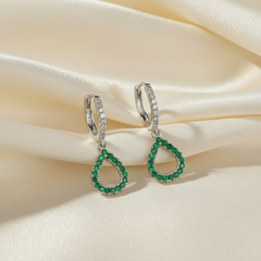 Pair of emerald green teardrop earrings on a beige satin background