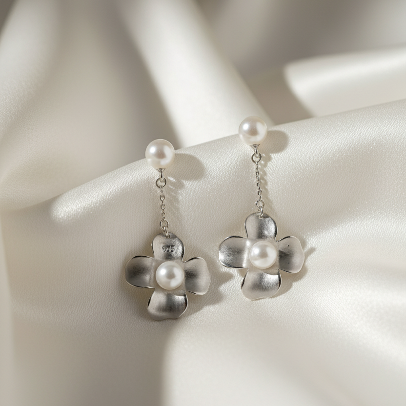 Silver flower-shaped earrings with pearl centers on a white satin background